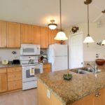 A Fully Loaded Kitchen Features - White full-sized refrigerator, hanging pots and pans for cooking, a full size stove, microwave, and granite countertops create the luxurious living you desire.